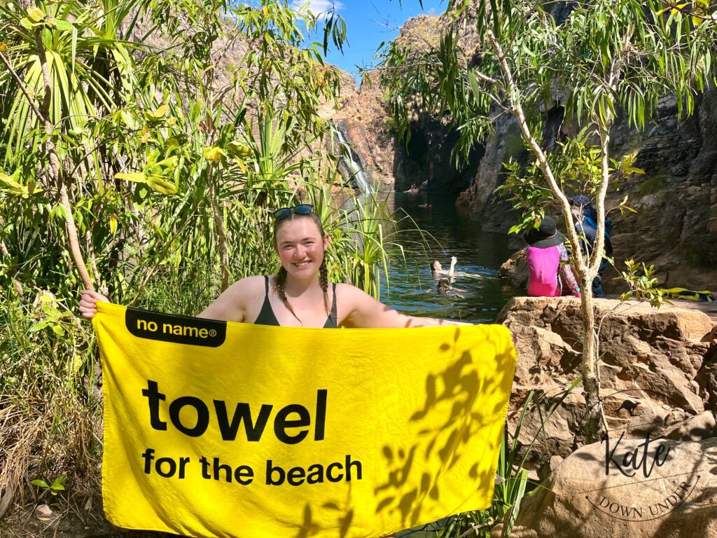 Kate holding up a yellow beach towel that reads "towel for the beach" at Maguk plunge pool