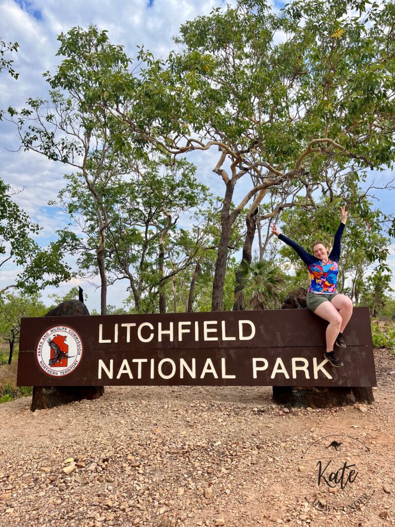 Kate sitting atop the Litchfield National Park sign with her hands up in the air showing 'peace' signs