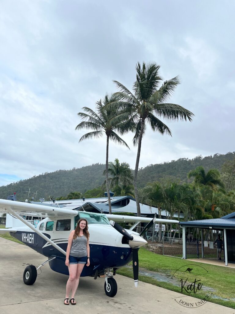 Kate standing next to the plane she had the scenic flight in, with two palms in the background