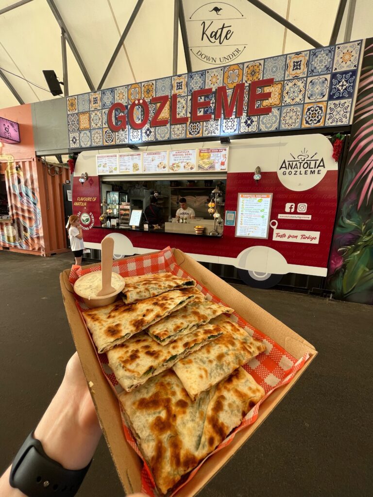 holding a spinach and feta gozleme in front of the stand it was purchased from
