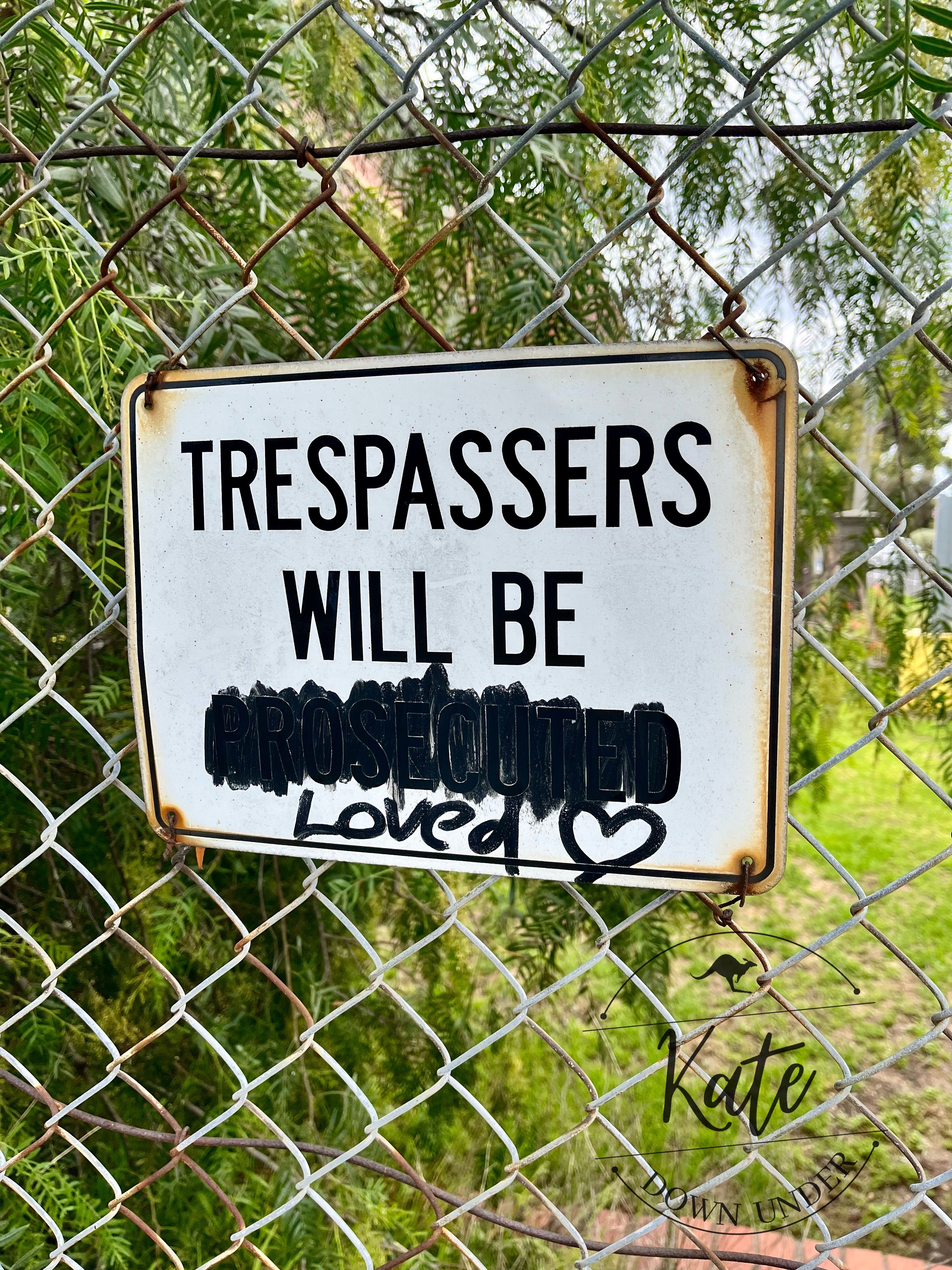 a sign posted on a chain link fence that originally read "trespassers will be prosecuted" but now reads "trespassers will be loved"