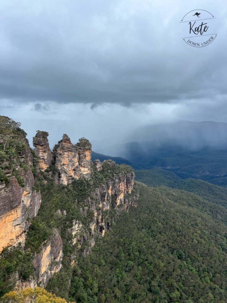 Three Sisters rock formation with clouds pouring rain approaching in the background