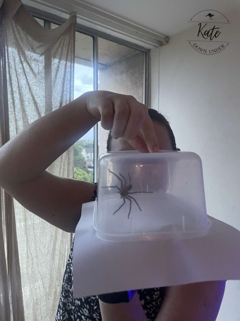 Kate holding a spider trapped in a clear plastic container with a sheet of paper