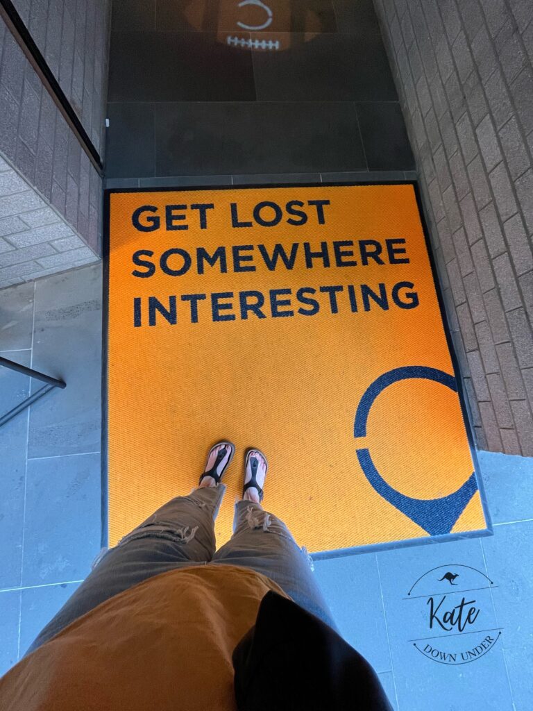 an orange entry way carpet that has a location pin and reads "get lost somewhere interesting" printed on it